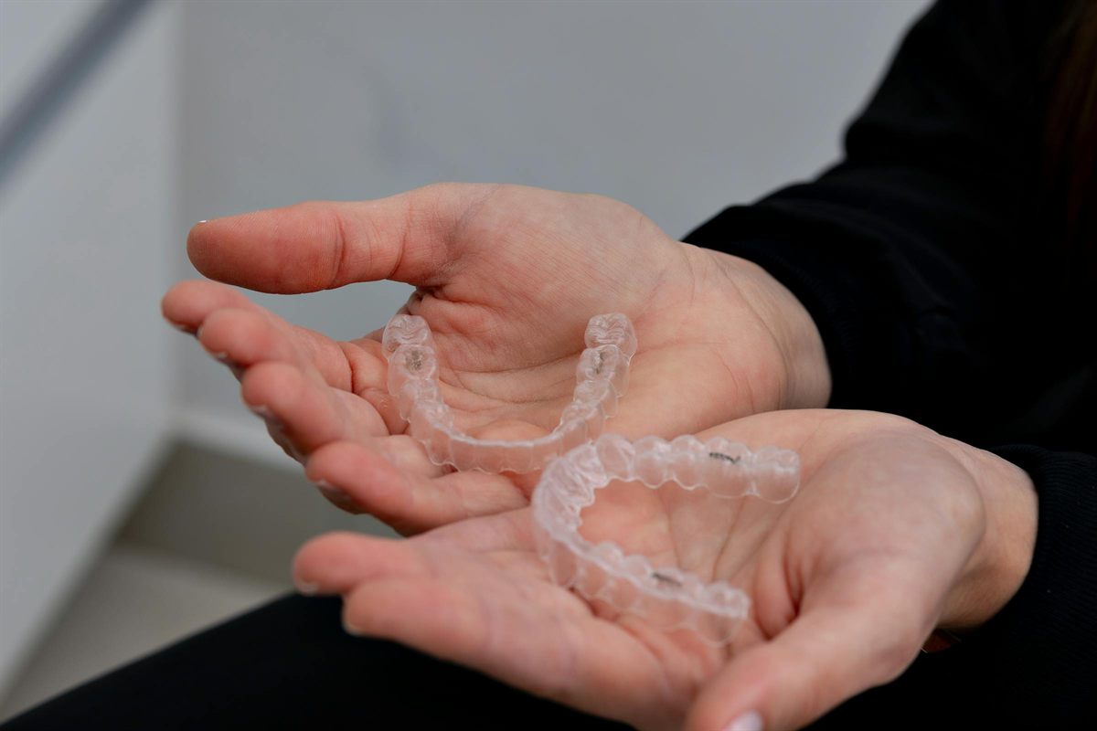 Alineadores Invisalign transparentes en su estuche junto a modelo dental con attachments
