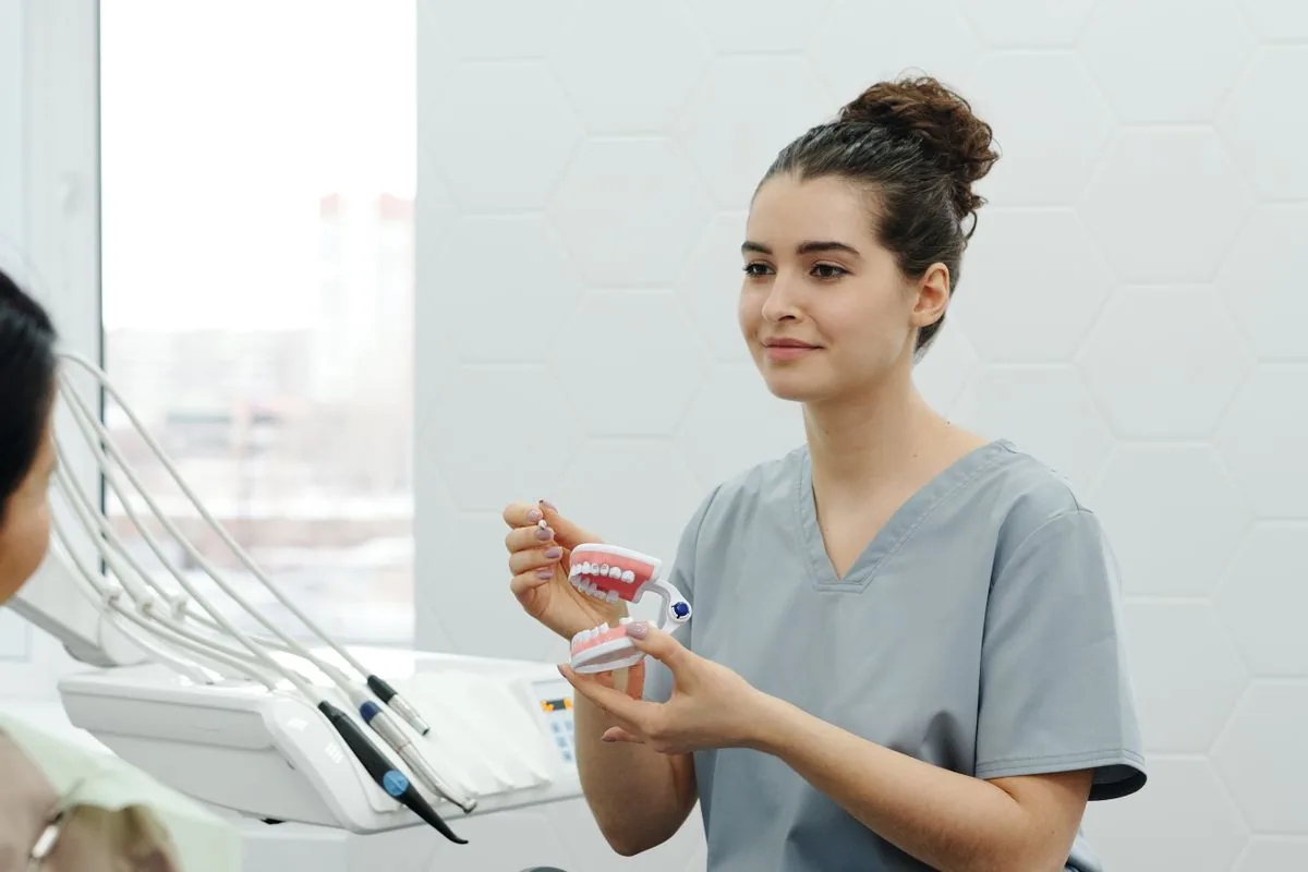 Odontóloga explicando a una paciente con un modelo dental si le conviene un implante o un puente
