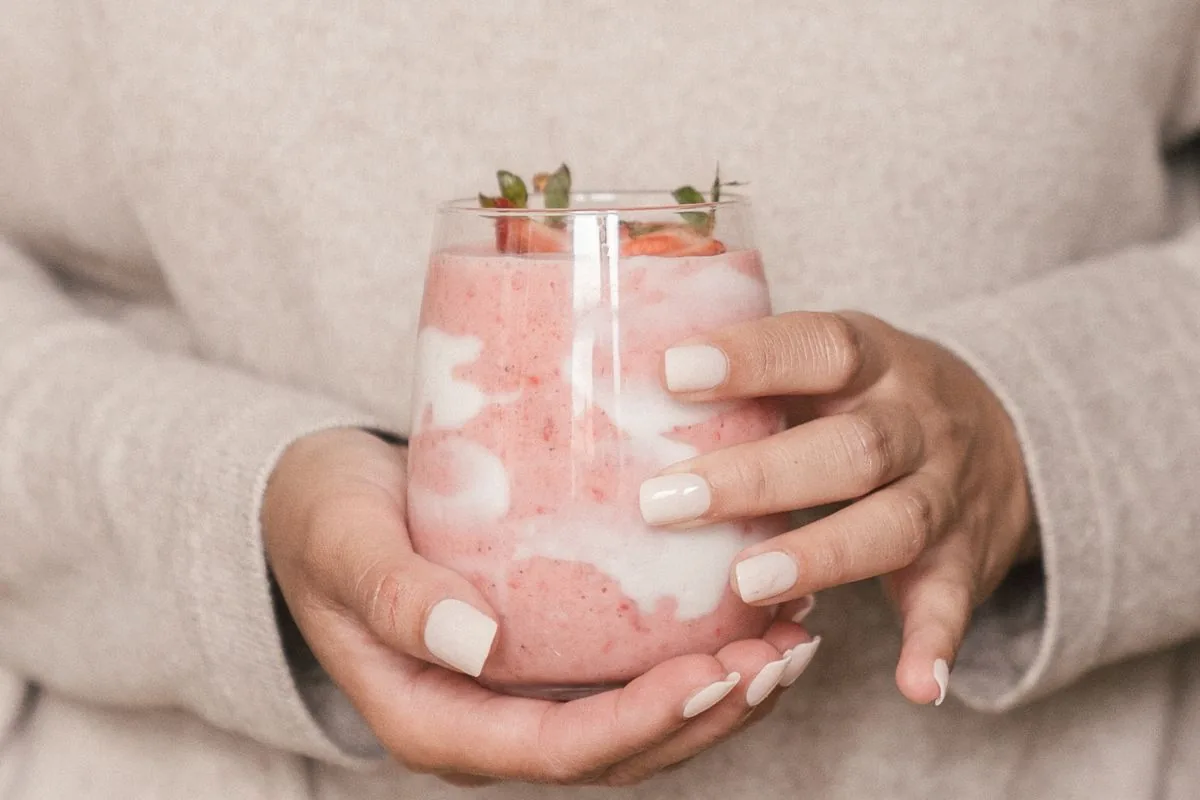 Manos sosteniendo un batido frío de fresa y yogur, parte de la dieta blanda para aliviar el dolor de brackets