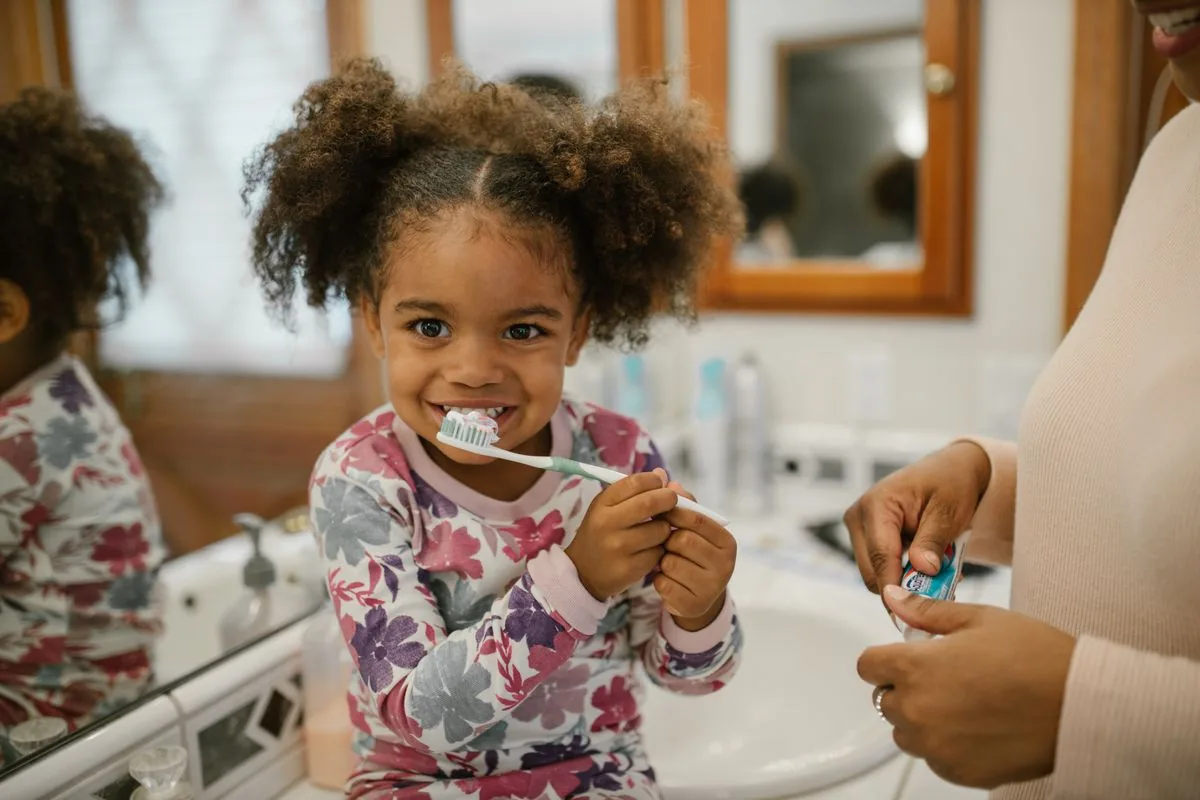 Niña cepillándose los dientes con la supervisión de un adulto para cuidar su mantenedor de espacio