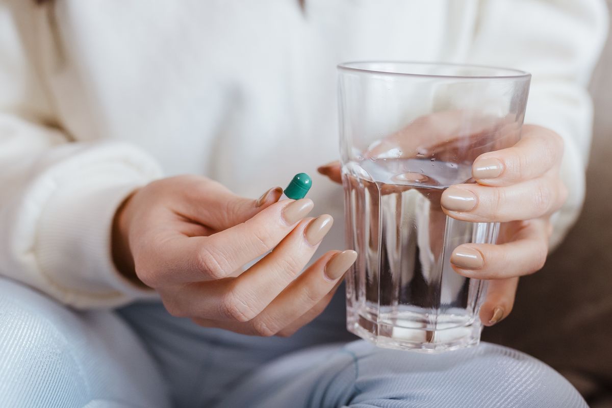 Persona tomando un analgésico con un vaso de agua después de sacar una muela del juicio